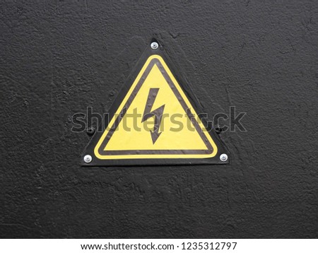 
High voltage sign, screwed to a rough black metal surface.					
