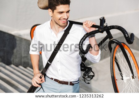 Image of a handsome young business man walking outdoors with bicycle.