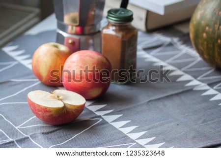 Red ripe apple and a white candle on gray tablecloth with nuts and coffee pot