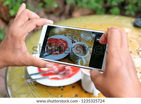 Woman's hand taking photo of slice of cheese cake and hot coffee on mobile phone while sitting in cafe, female looking and using cellphone during breaking and relaxing time 