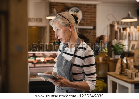 Mature coffee shop employee standing next to the fridges in the coffee shop performing a stock take.