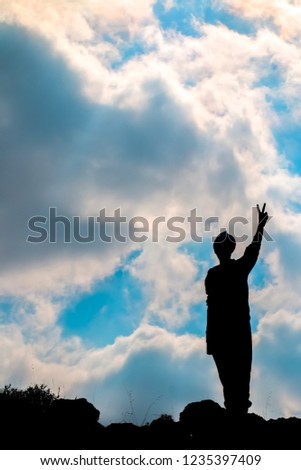 Silhouette of a man Raising the victory sign with clouds sky background. Conceptual scene.
