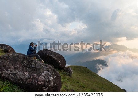 Young traveler photographer with photo camera sitting on the top of mountain and looking on the sunset