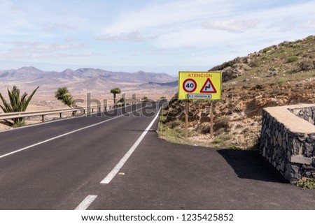 Curved road with sign Attention in Fuerteventura. Canary Islands, Spain