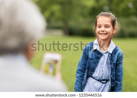 family, leisure and technology concept - happy little girl being photographed at summer park