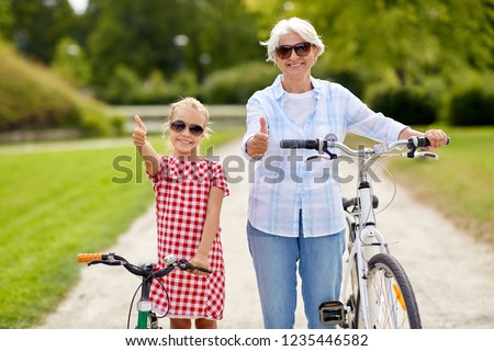 family, leisure and people concept - happy grandmother and granddaughter with bicycles showing thumbs up at summer park