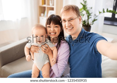 mixed race family, parenthood and people concept - happy mother and father with baby son taking selfie at home