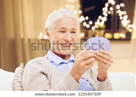 old age, gamble, holidays and people concept - happy smiling senior woman playing cards at home over garland lights background