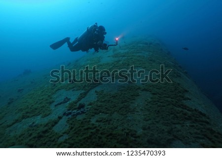 Scuba diver exploring deep shipwreck. Diver with underwater camera swimming over the sunken ship. Corals on the hull of the wreck. Picture of the scuba diver explorer.