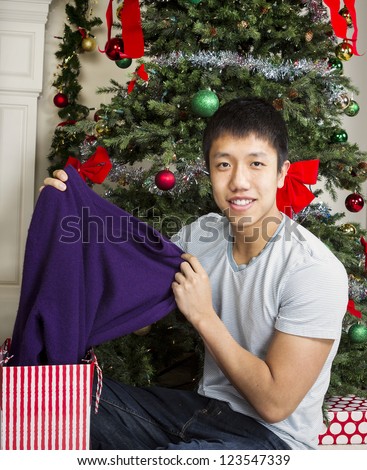 Young Adult man pulling out purple sweater from bag with Christmas tree in background