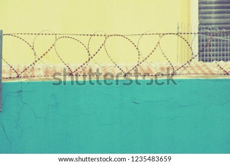 Barbed wire in the shape of abstract hearts on a blue wall with a light yellow background.