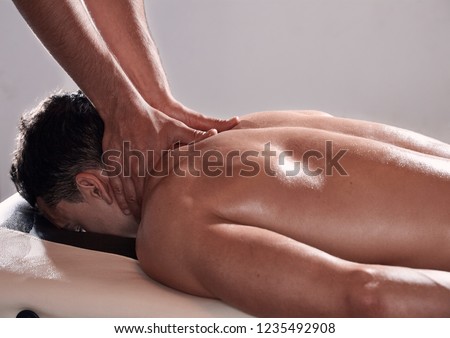 side view, two young man, 20-29 years old, sports physiotherapy indoors in studio, photo shoot. Physiotherapist massaging relaxed patient neck back side, with his hands.