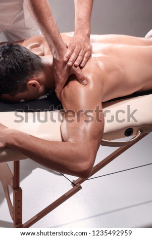 elevated view, two young man, 20-29 years old, sports physiotherapy indoors in studio, photo shoot. Physiotherapist massaging patient shoulder with his hands.
