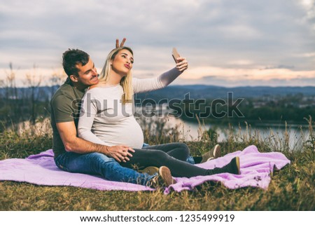 Happy husband and his pregnant wife taking selfie while they enjoy spending time together outdoor.Toned image.