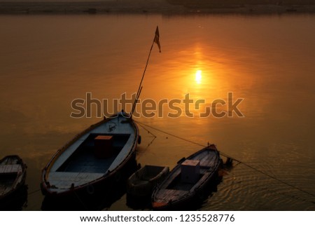 Beautiful sunset on the calmness Ganges river and boats moored to the shore. One of the vessel has a primitive archaic form of a freaking boat