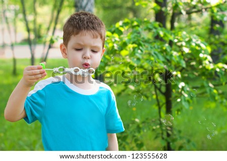 Little boy blowing soap bubbles in summer park