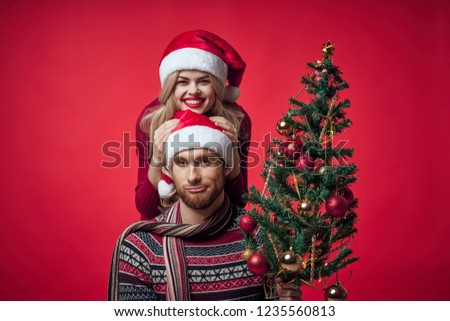 woman on a red background stands behind a man with a Christmas tree in his hand                 
