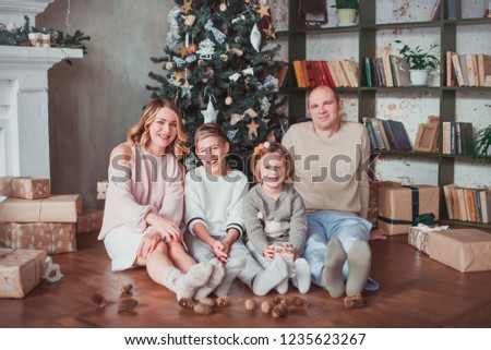 Happy family sitting on the wooden floor in the room next to the Christmas tree. They laugh. On the floor are cones. Warm colour. New year concept