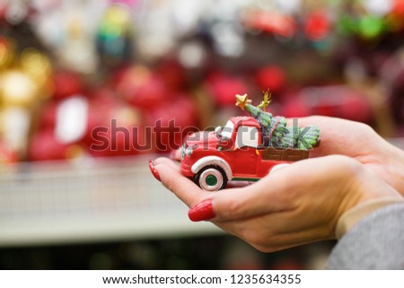 girl holding in her palms a toy of a red New Year's car with a New Year tree