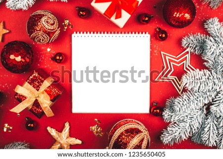 White square notebook and glittering Christmas decorations on red background. Flat lay style. Planning concept.