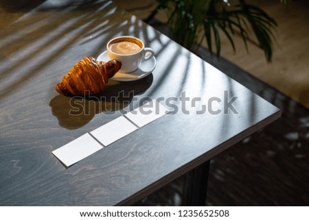 Close up of coffee cup, croissant and business cards on dark wooden table.