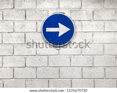 white arrow on blue road sign hanging on wall pointing right direction