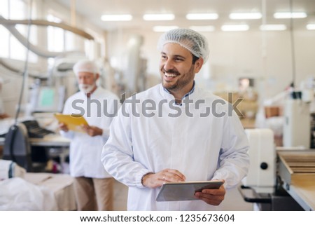 Smiling man using tablet while standing in food factory.