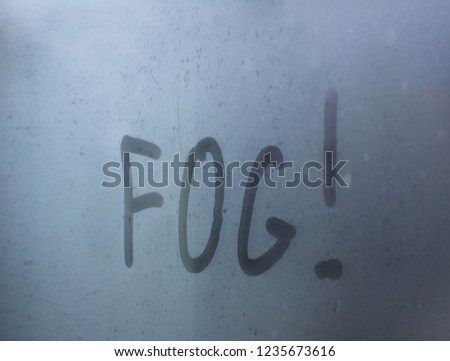 The inscription - "fog" written by a finger on a misted glass with mkrymi drops. Warning motorists about the dangers on the roads. Traffic safety. Weather forecast. White shroud outside the window.
