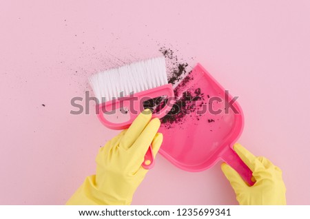 Top view. Flat lay photography female hands in yellow latex gloves with brush and dustpan clean the dirt on pink background. Copy space. Mock up.