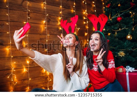 Smiling girlfriends taking a selfie with smarphone. Christmas mood.