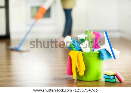 Cleaning items on floor in modern kitchen. Woman maid or charwoman blured in background. Bucket, brush, washcloth, spray. Royalty-Free Stock Photo #1235754766
