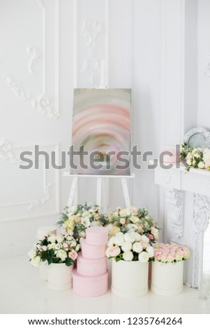 Elegant white fireplace full of flowers. Elegant white room decorated with easel and hat boxes. Wedding decorated area. Vintage decor in light interior