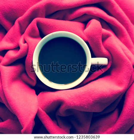 Photo of a cup with a black coffee and a soft red scarf. Cute composition with coffee.