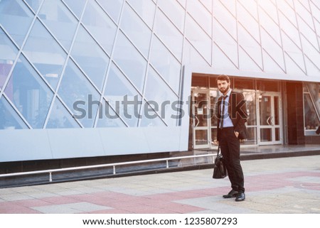 Modern businessman with bag on skyscraper background.
