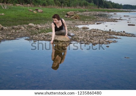 young woman on a wild shore scoops water with her palm from the lake