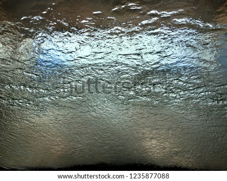 Light rays shining through Water sheeting pouring down glass window, windshield windscreen view through dry side while going through car wash, to create background textural cool image, resembling ice