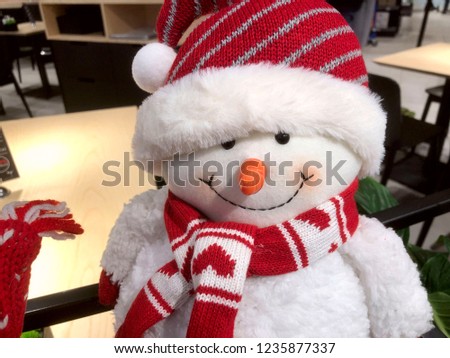 White toy snowman with a red scarf and a red bright hat. Soft white fun toy on the table. Cropped shot, close-up. Christmas concept.