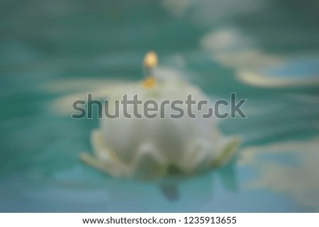 The blur of the white lotus floats in the water , candle on the top of the lotus.