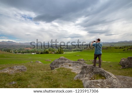 A male tourist takes a photo of the landscape at Elephant Rocks, in the Waitaki Valley, New Zealand, with his  cellphone 