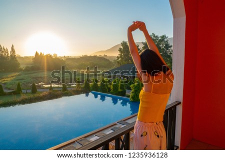  young girl stretch oneself in the morning at terrace pool&mountain view and looking beautiful sunrise  Royalty-Free Stock Photo #1235936128