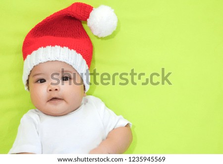 Newborn Asian baby is wearing red Christmas knitting hat and white dress on light green background