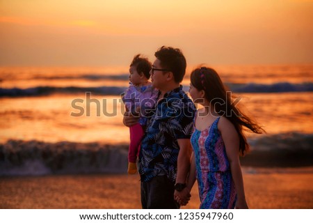 young happy and beautiful Asian Chinese couple holding baby girl daughter walking on sunset beach enjoying together romantic summer holidays trip in family sweet vacations concept