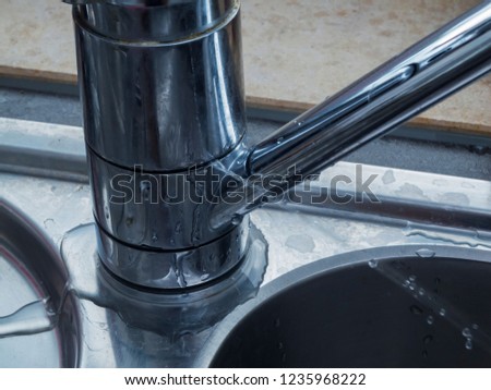 Close-up of a leaking faucet with jetting out the jet of water on a sink at the window.