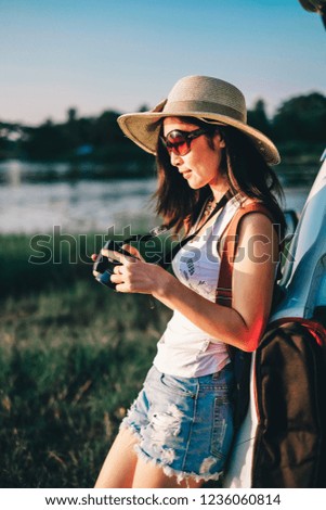 Asia woman photographer standing near hatchback car and taking photo  near the lake on holiday.beautiful tourist watch view of nature on vacation.