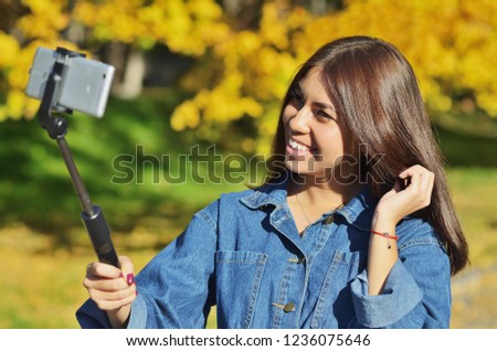 A young beautiful girl in a denim suit takes a selfie walking in the city Park in the autumn, horizontal photo