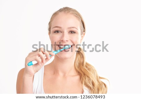 Studio shot of beautiful young woman brushing her teeth while looking at camera and smiling. Isolated on white background. 