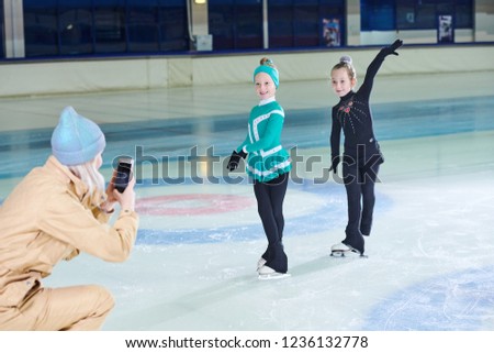 Full length portrait of two smiling  little figure skaters posing for photograph in indoor rink, copy space