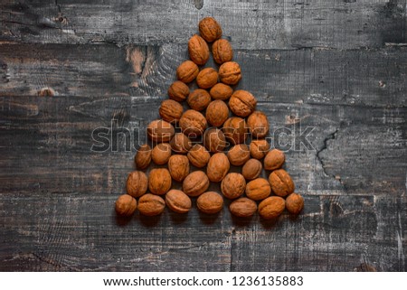 A few walnuts on an old wooden table or wooden surface are laid out in the shape of a Christmas tree. Layout top view