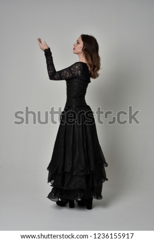 full length portrait of brunette  girl wearing long, black lace ball gown. standing pose on grey studio background.