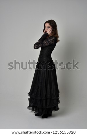 full length portrait of brunette  girl wearing long, black lace ball gown. standing pose on grey studio background.